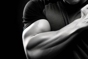 A man is posing in front of a black background, showcasing his biceps.