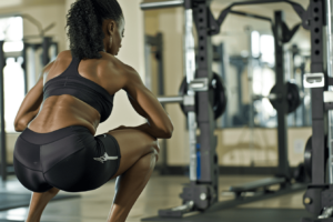 A woman performing squats in a gym, focused on strengthening her glutes beside weightlifting equipment.