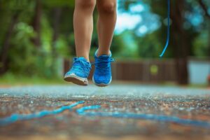 Child in blue sneakers about to jump rope over a chalk-drawn line on a pavement.