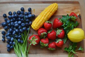 Fresh blueberries, strawberries, a corn cob, green onions, parsley, and a lemon artfully arranged on a wooden cutting board debunk common nutrition myths.
